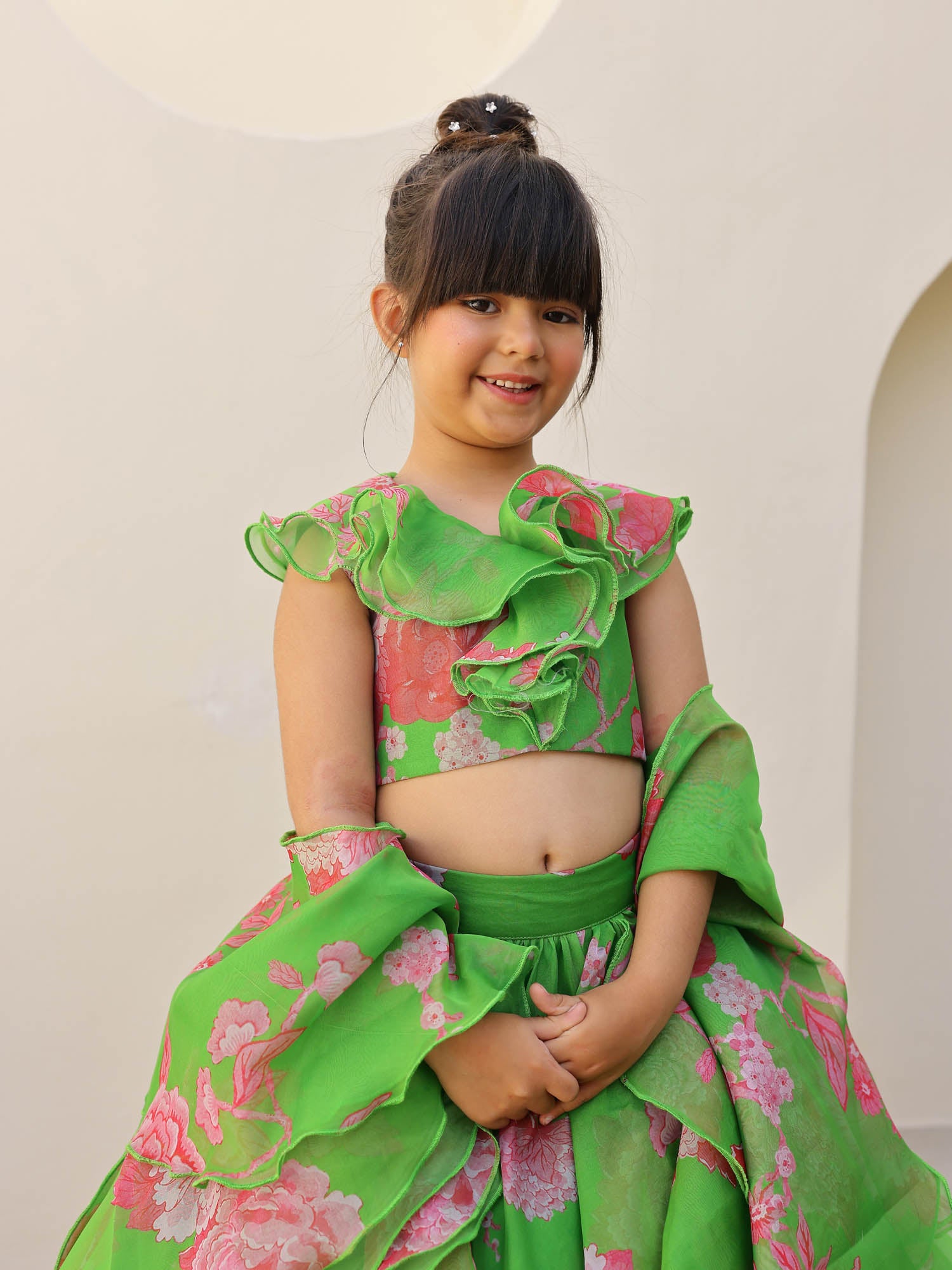 Close-up of a child in a green and pink floral printed organza lehenga featuring a ruffled neckline and matching dupatta.
