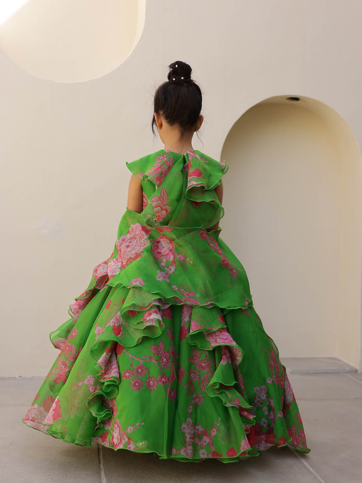 Full-length view of a girl twirling in a soft green floral organza lehenga with cascading ruffles and pink flower motifs.