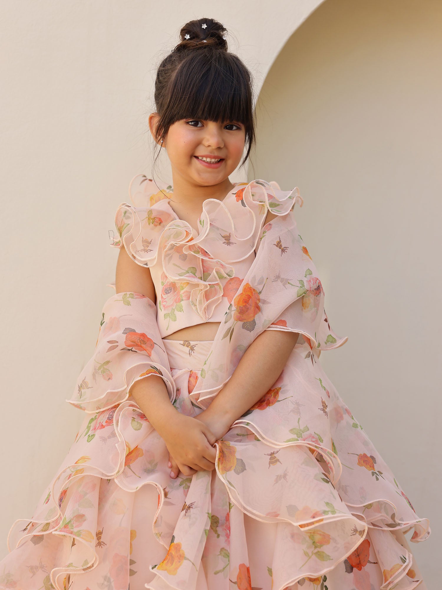 Child dressed in a peach ruffle lehenga set featuring a floral-printed blouse and matching organza dupatta.