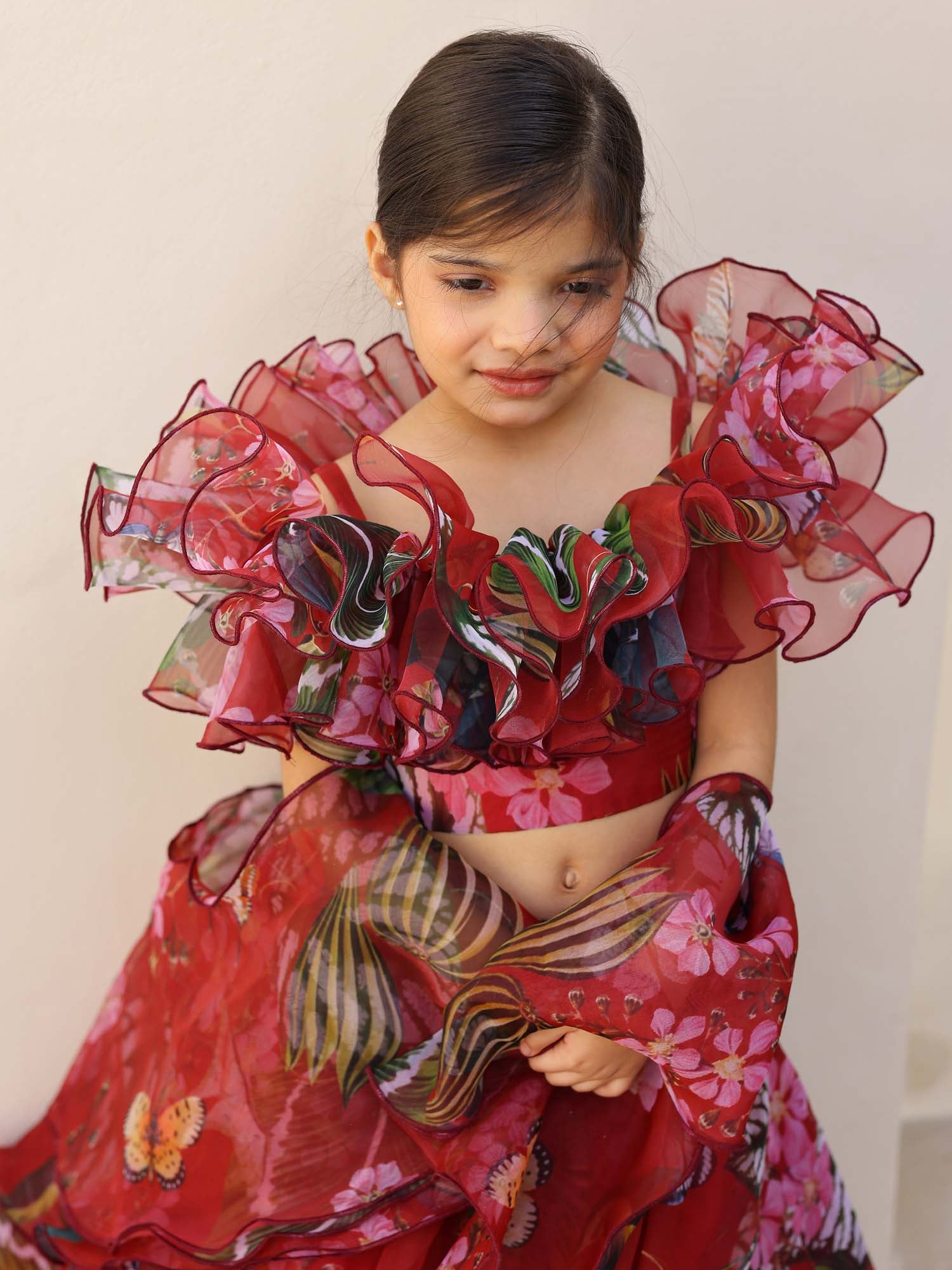 Child dressed in a red ruffle lehenga featuring floral and leaf motifs with matching dupatta.