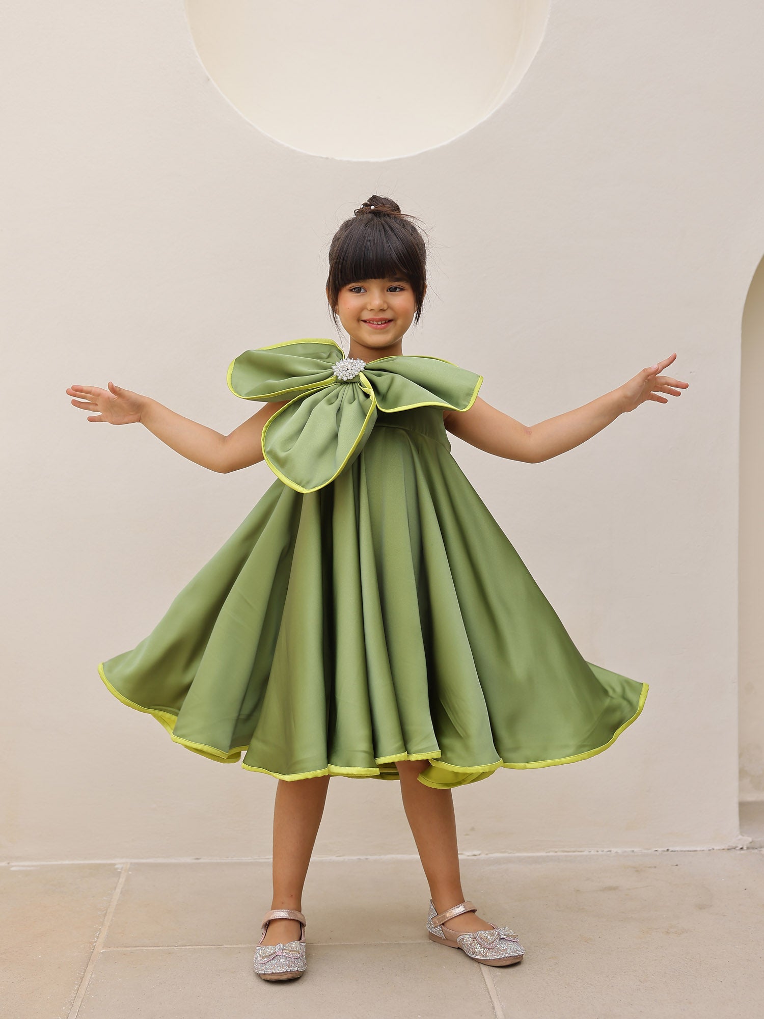 Child wearing a green dress with a large bow .